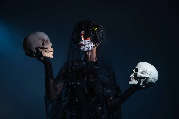 Mujer en el tradicional día mexicano de maquillaje muerto y disfraz sosteniendo calaveras sobre fondo azul oscuro - foto de stock