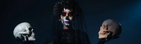 Mujer en disfraz de Halloween espeluznante y maquillaje celebración de calaveras sobre fondo negro y azul, bandera - foto de stock