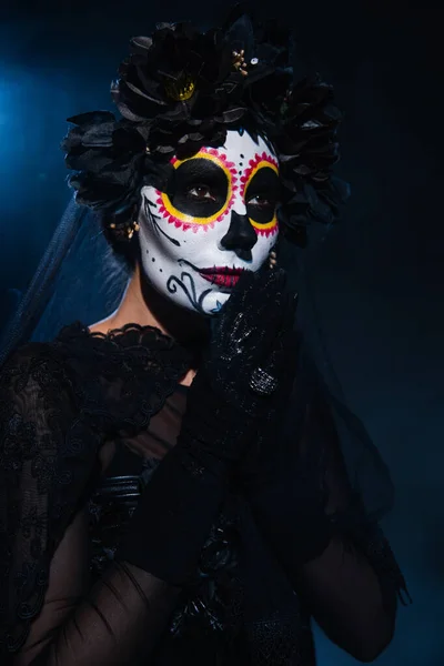 Frau mit Halloween-Zuckerschädel-Make-up und betenden Händen, die vor dunkelblauem Hintergrund wegschauen — Stockfoto