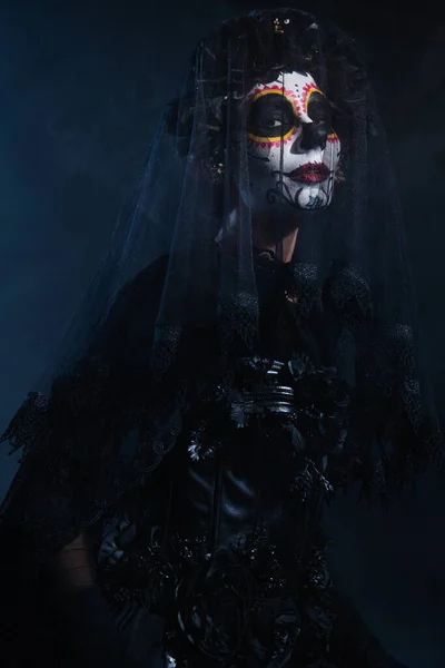 Woman in traditional santa muerte makeup and black lace veil looking at camera on dark blue background — Stock Photo