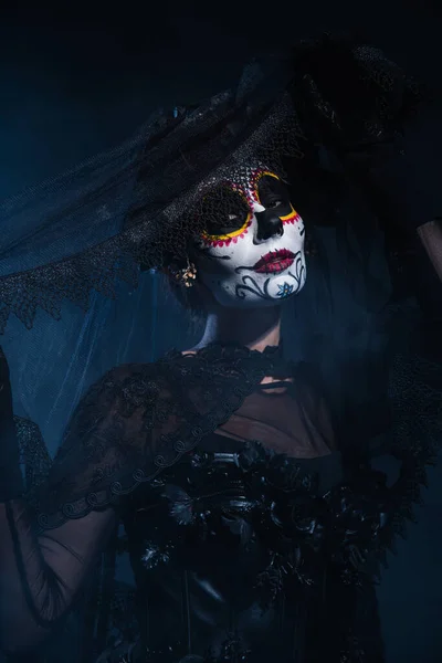 Жінка в костюмі Хеллоуїна і моторошний макіяж позує з чорною мереживною завісою на темно-синьому фоні — стокове фото