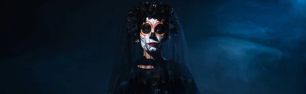 Woman in mexican day of dead makeup and black wreath with veil on dark background with blue smoke, banner — Stock Photo