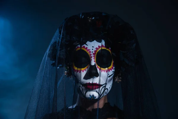 Portrait of woman with closed eyes and scary halloween makeup wearing black wreath and veil on blue foggy background — Stock Photo