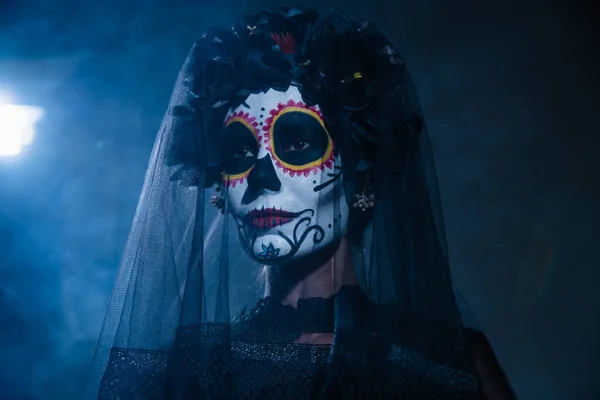 Porträt einer Frau in gespenstischem Halloween-Make-up und schwarzem Kranz mit Schleier auf dunklem Hintergrund mit blauem Licht — Stockfoto