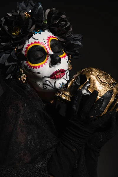 Mujer con el maquillaje de Halloween miedo y los ojos cerrados celebración de cráneo de oro aislado en negro - foto de stock