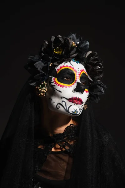 Retrato de mujer con maquillaje espeluznante halloween y corona oscura mirando hacia otro lado aislado en negro - foto de stock