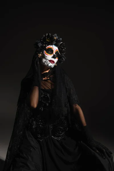 Femme en costume effrayant et jour mexicain de maquillage mort assis sur fond noir — Photo de stock