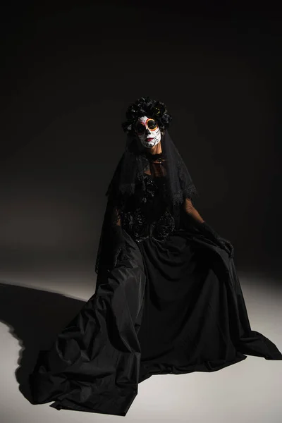 Comprimento total da mulher em vestido preto e com maquiagem assustadora halloween no fundo escuro — Fotografia de Stock