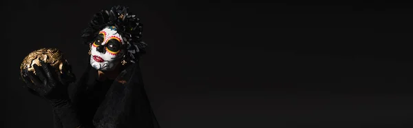 Femme en costume santa muerte et maquillage catrina tenant le crâne doré isolé sur noir, bannière — Photo de stock