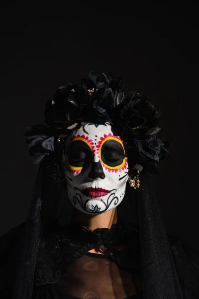 Portrait of woman with closed eyes in scary catrina makeup and dark wreath isolated on black — Stock Photo