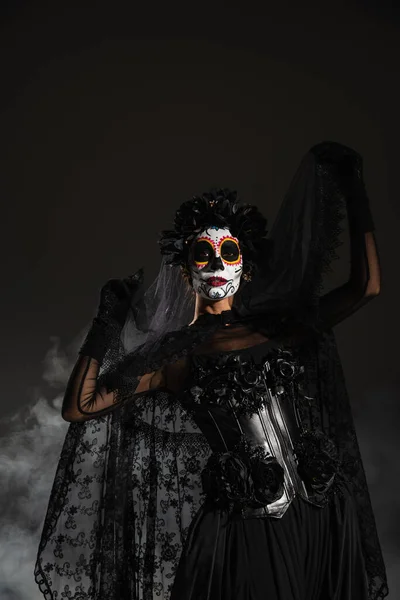 Mulher no dia mexicano tradicional de maquiagem morta posando com véu de renda preta no fundo escuro fumegante — Fotografia de Stock