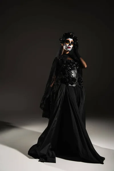 Volle Länge der Frau in Zucker Totenkopf Make-up und dunkles Kleid mit Schleier auf schwarzem Hintergrund — Stockfoto