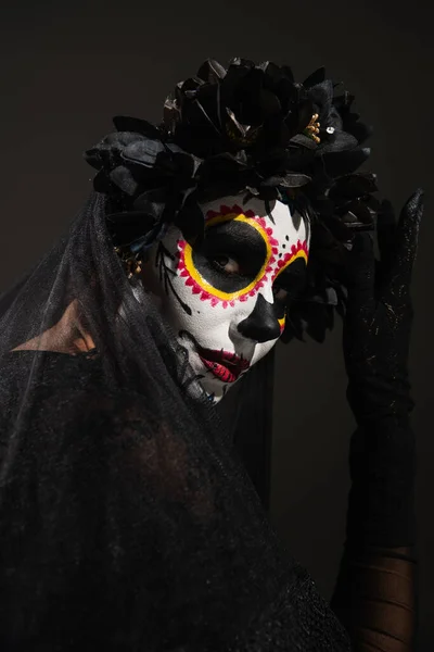 Portrait of woman in sugar skull halloween makeup and dark wreath with veil looking at camera isolated on black — Stock Photo