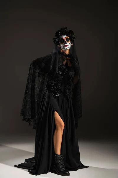 Piena lunghezza della donna in zucchero cranio trucco posa in costume nero Halloween su sfondo scuro — Foto stock