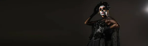 Mujer en el maquillaje de Halloween espeluznante y traje de bruja oscura sobre fondo negro, bandera - foto de stock