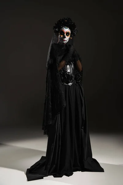 Повна довжина жінки в сумному костюмі і мексиканський день мертвого макіяжу, що стоїть на чорному тлі — стокове фото