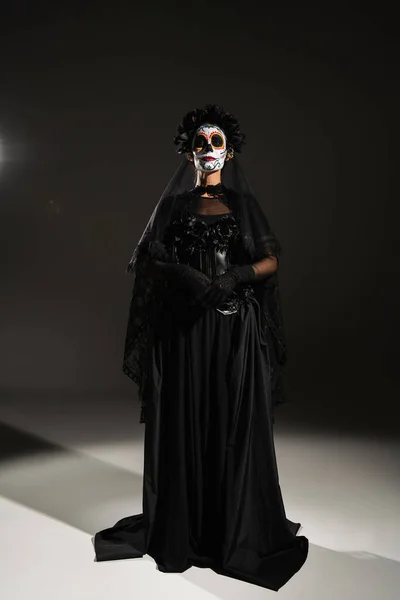 Vista frontal de la mujer en traje espeluznante negro y maquillaje de Halloween sobre fondo negro - foto de stock
