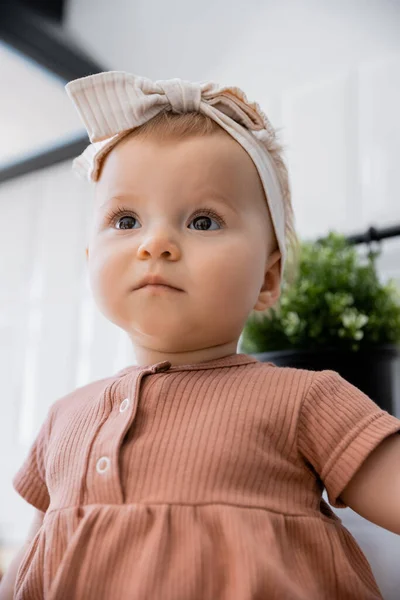 Portrait of infant baby girl in headband with bow and pink dress looking away — Stock Photo