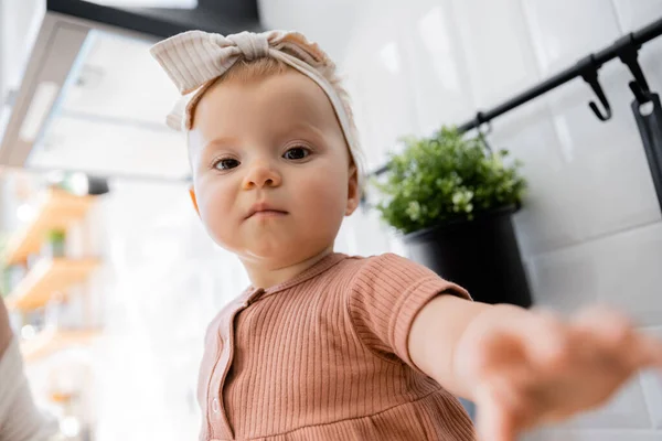 Portrait of infant baby girl in headband with bow sitting with outstretched hand and looking at camera — Stock Photo