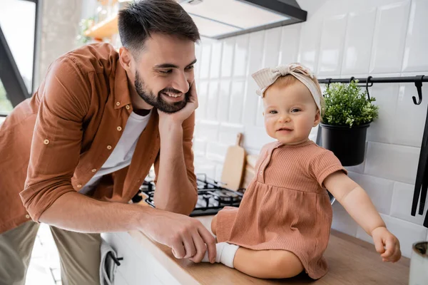 Счастливый бородатый мужчина трогает крошечную ножку дочки, сидящей на кухонном столе — стоковое фото