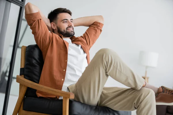 Homem feliz e barbudo sentado em poltrona de couro confortável na sala de estar — Fotografia de Stock