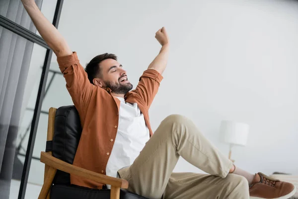 Uomo barbuto allungamento e sbadigliare mentre seduto su comoda poltrona in pelle in soggiorno — Foto stock