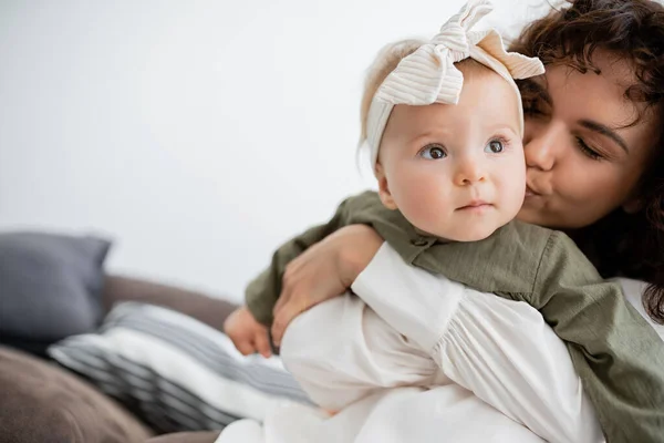 Mère bouclée étreignant et embrassant la joue de bébé fille dans le bandeau — Photo de stock