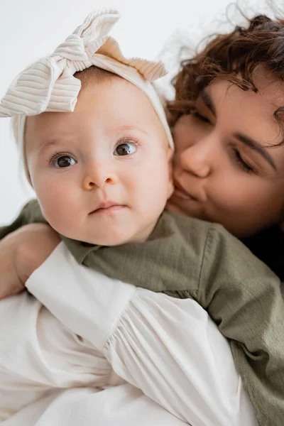 Крупним планом кучерява мати обіймає і цілує щоку немовляти в пов'язці — стокове фото