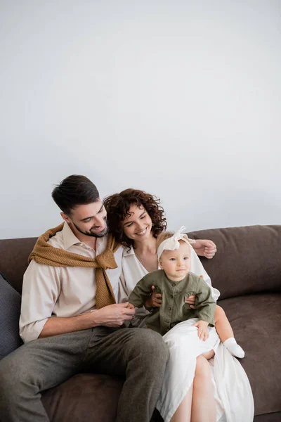 Genitori felici guardando neonata in fascia mentre seduto sul divano in soggiorno — Foto stock