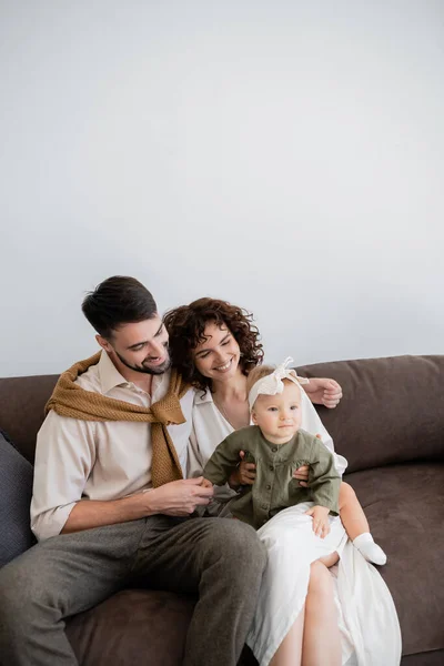 Padres felices mirando a la niña en diadema mientras está sentada en el sofá en la sala de estar - foto de stock