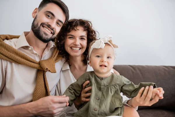 Веселые родители и малышка смотрят в камеру, сидя на диване в гостиной — Stock Photo