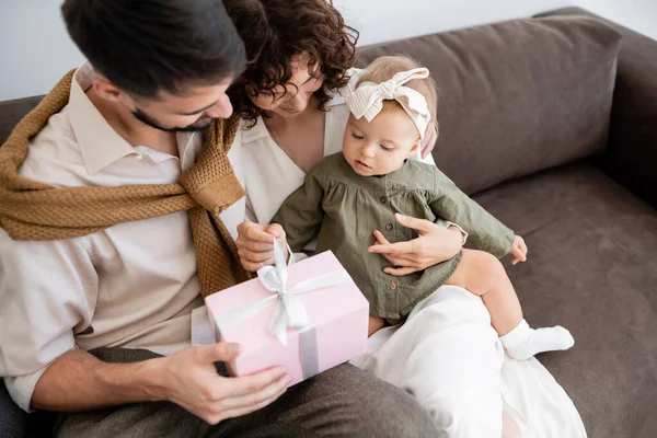 High angle view of happy parents holding gift box near baby girl in headband — Stock Photo