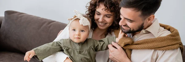 Genitori positivi guardando la neonata in fascia in soggiorno, striscione — Foto stock