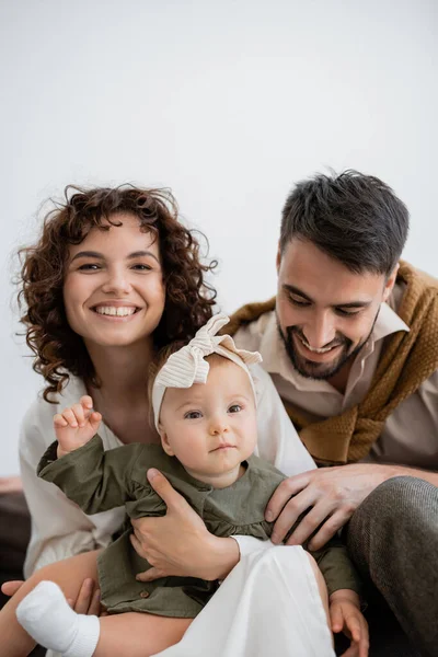 Pais positivos segurando menina infantil na cabeça e sorrindo na sala de estar — Fotografia de Stock