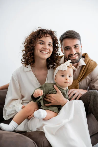 Pais positivos segurando bebê menina na cabeça e sorrindo na sala de estar — Fotografia de Stock