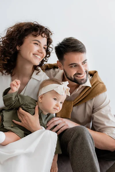 Padres satisfechos sosteniendo niña en diadema y sonriendo en la sala de estar - foto de stock