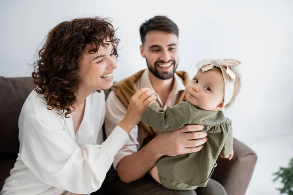 Marito e moglie felici che tengono la bambina in fascia e sorridono in soggiorno — Foto stock