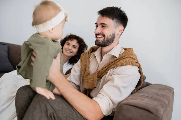 Pai alegre segurando criança filha perto feliz esposa turva na sala de estar — Fotografia de Stock