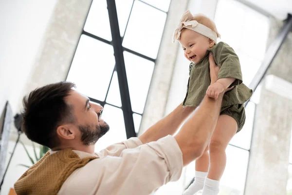 Alegre padre sosteniendo positivo bebé hija en diadema y vestido - foto de stock