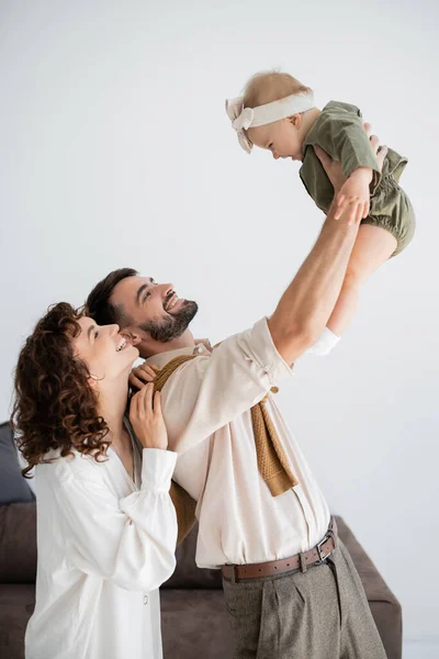 Веселий молодий батько тримає в руках немовляти дочку біля щасливої дружини — стокове фото