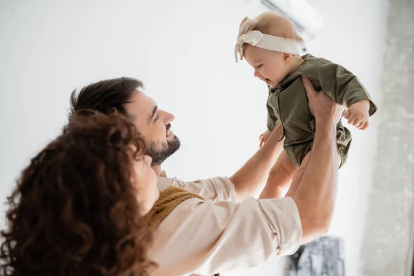 Joyful husband and curly wife holding baby girl in headband and dress — Stock Photo