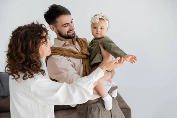 Marido satisfeito e encaracolado esposa segurando bebê menina na cabeça e vestido — Fotografia de Stock