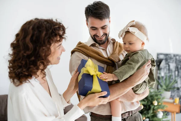 Glückliche Mutter hält Geschenkbox in der Nähe Ehemann hält Säugling Mädchen an Weihnachten — Stockfoto
