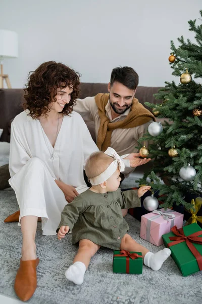 Happy family with infant baby girl sitting near christmas tree with presents — Stock Photo