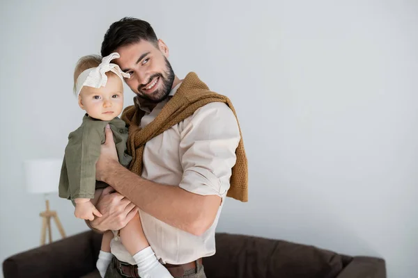 Cheerful bearded man holding in arms baby girl in dress and headband — Stock Photo