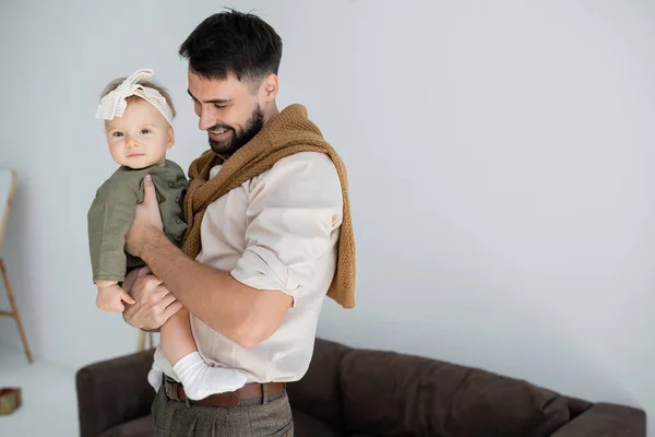 Positive bearded father holding in arms infant daughter in dress and headband — Stock Photo