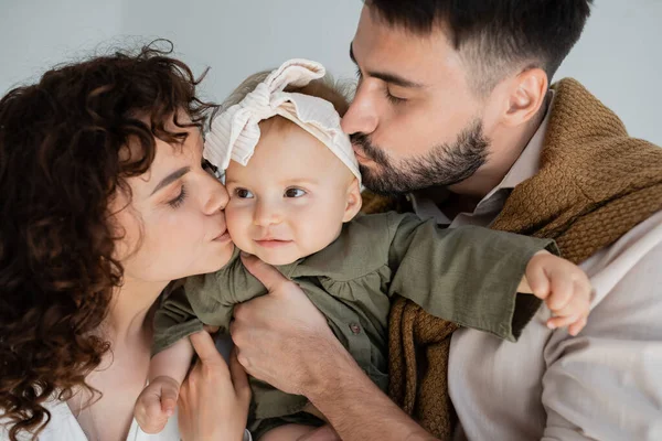 Uomo barbuto e donna riccia baciare le guance della bambina in fascia — Foto stock