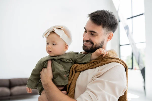 Hombre barbudo alegre sosteniendo en brazos y mirando al bebé en diadema - foto de stock