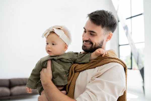 Cheerful bearded man holding in arms and looking at infant baby in headband — Stock Photo