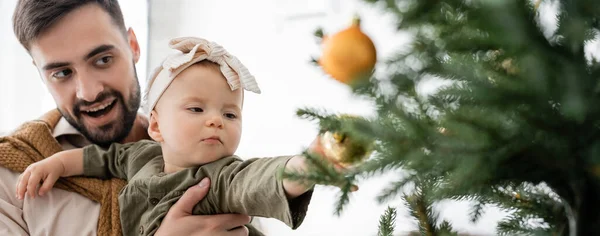 Padre eccitato che tiene la figlia neonata vicino all'albero di Natale decorato, banner — Foto stock
